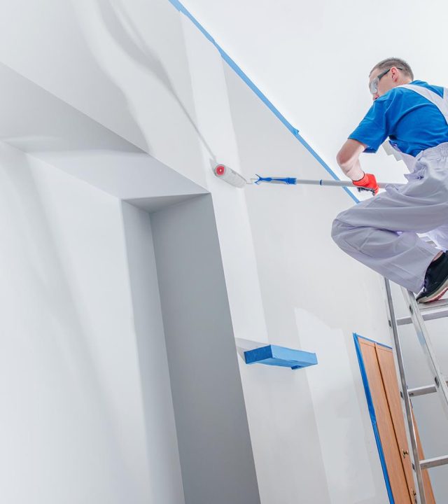 House Painting Business House Painting and Renovation Business Concept. Caucasian Male Painting House Room From the Ladder.
